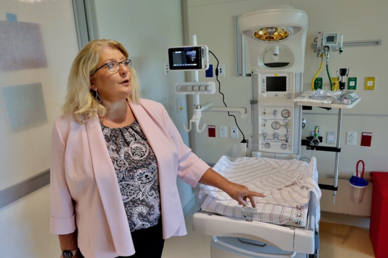 Sharon Kurfuerst stands beside a newborn bed in a labor and delivery room