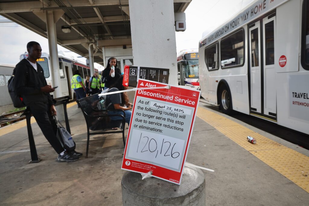 People waiting for buses at the station, with a sign alerting passengers about 2 routes that are discontinued