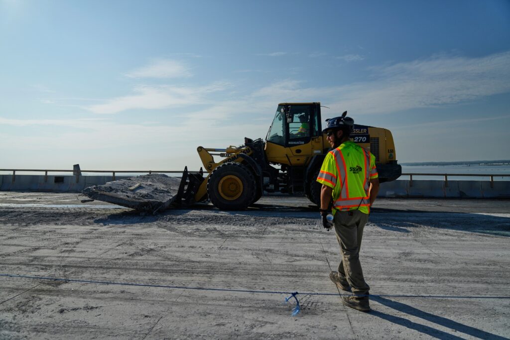 baltimore-bridge-repair-2025-07-30 A demolition crew member walking toward a bulldozer