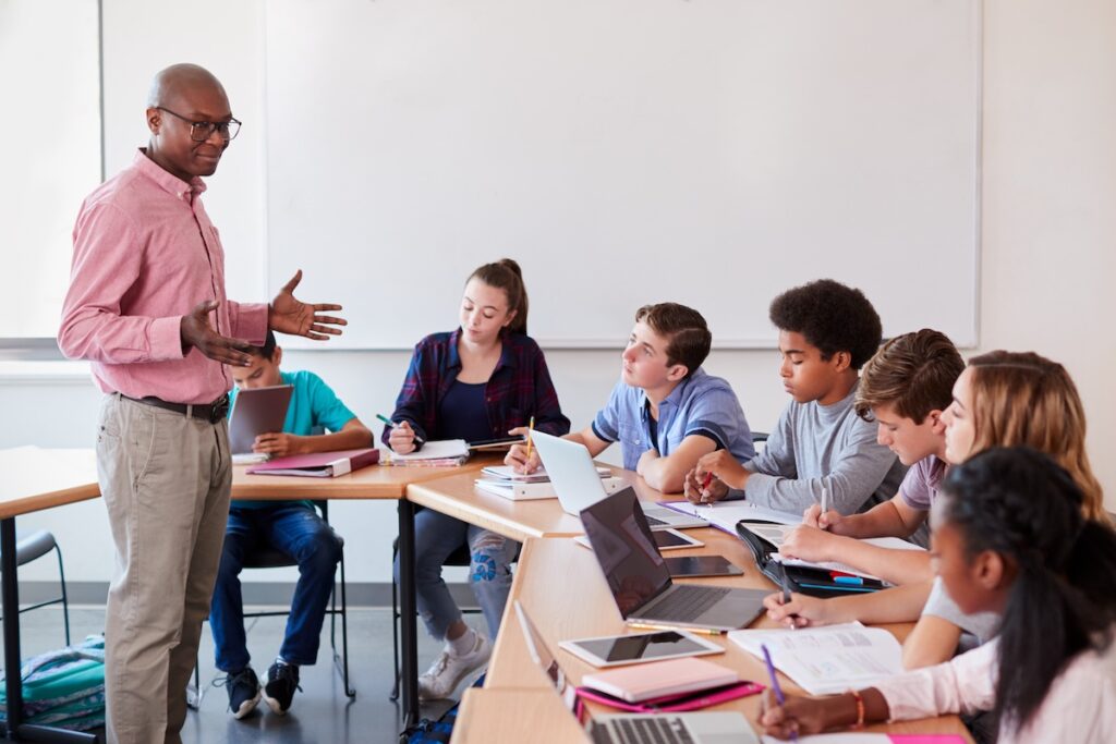 A high school teacher talking to students who are using technology in class. (Bigstock Image)