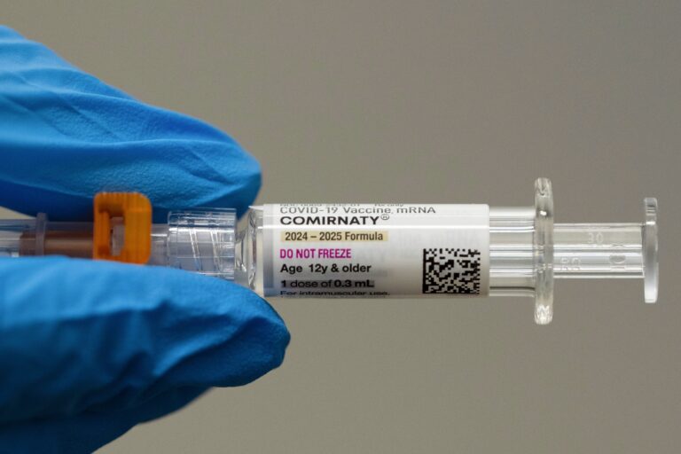 Someone wearing blue gloves holding a needle with a vaccine shot