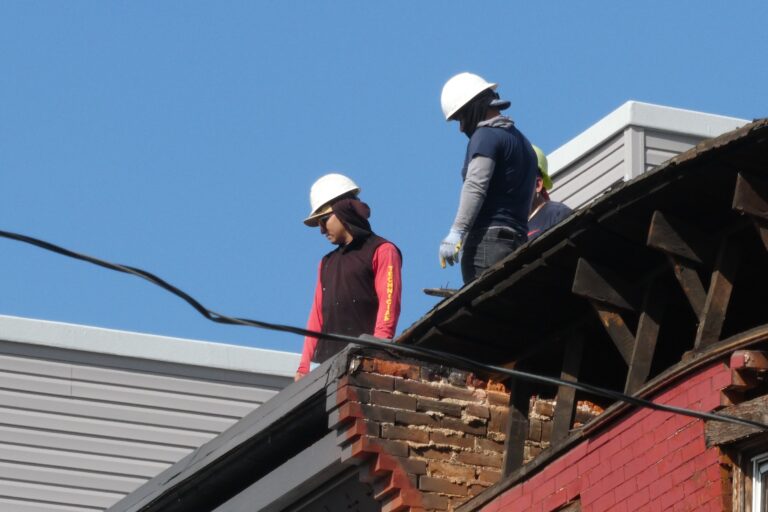 two workers on top of a roof near a collapsed Philadelphia house