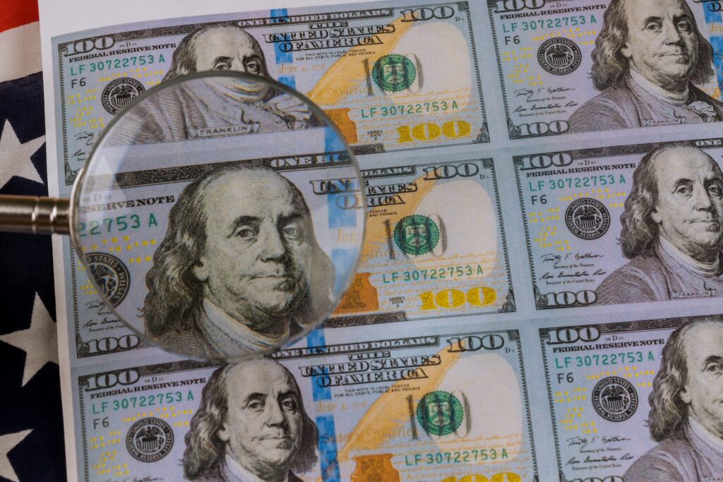 Winking Benjamin Franklin on hundred US dollars bill for magnifying glass A magnifying glass is seen over stacks of bills
