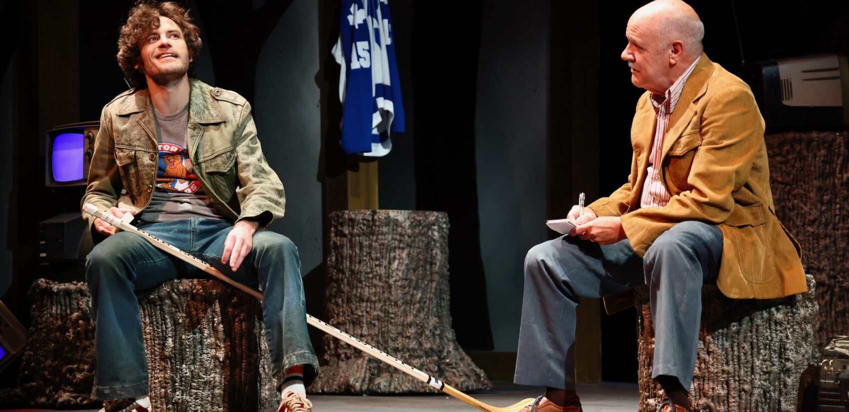 Two men talking while stiting down. One of them is holding a hockey stick