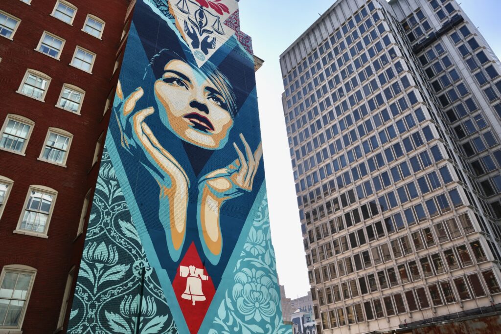 ''Uplift Justice'' by Shepard Fairey, a mural featuring a woman's face and her hands held up below her chin, is painted on the side of a Center City office building on Arch Street