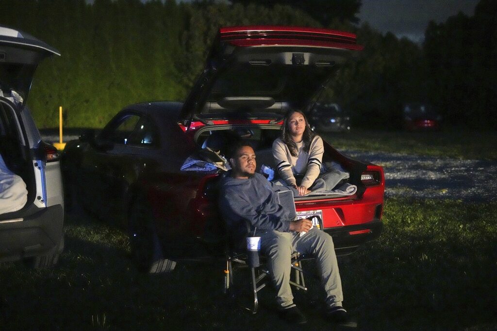 A couple watch a movie at a drive-in theater in the back of a car