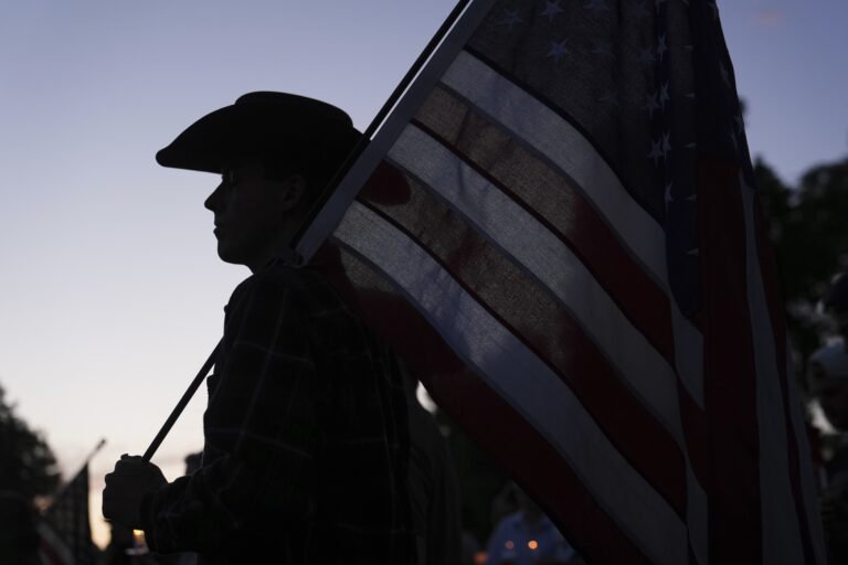 A silhouette of a man wearing a cowboy hat holding a large American flag