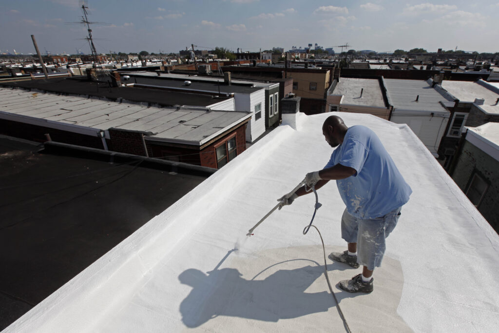 Homes Cool Roofs a worker applies a coating of Acrymax to the roof of a rowhouse in Philadelphia