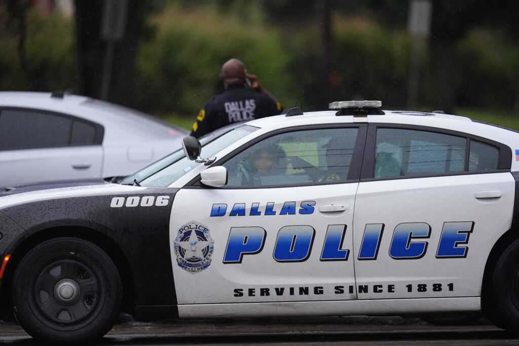 Immigration-Facility-Shooting An officer stands behind a Dallas Police Department car in the middle of the street