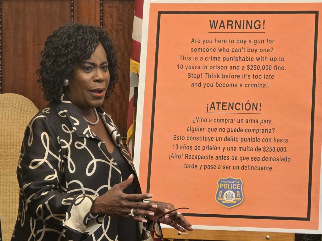mayor-cherelle-parker-gun-straw purchase-regulations-2025-09-08 Mayor Cherelle Parker next to a board reading, in Spanish and English, WARNING! Are you here to buy a gun for someone who can't buy one? This is a crime punishable with up to 10 years in prison and a $250,000 fine. Stop! Think before it's too late and you become a criminal.