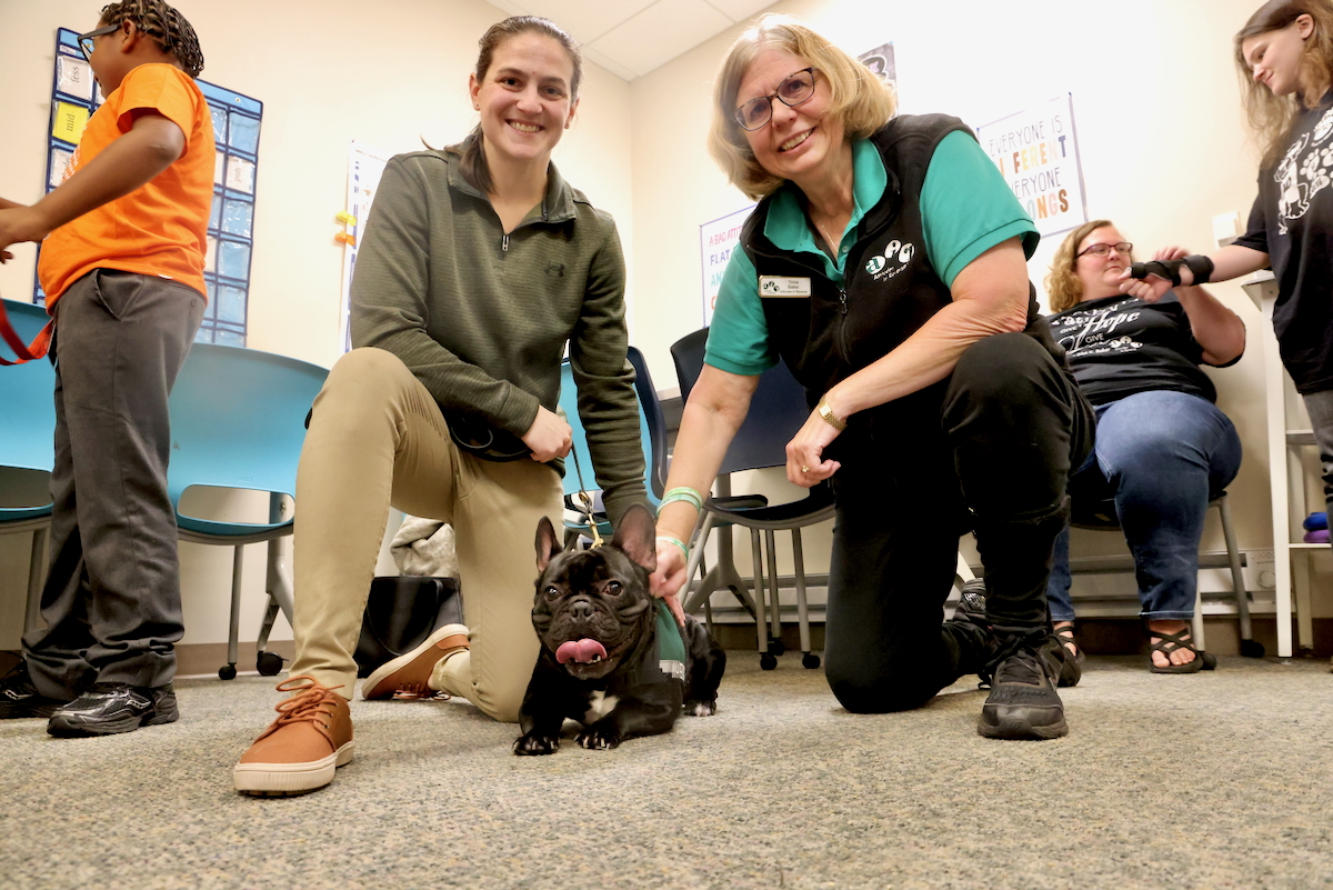 Samantha Sarin, Tricia Baker and Maverick, a String Theory School therapy dog, smile