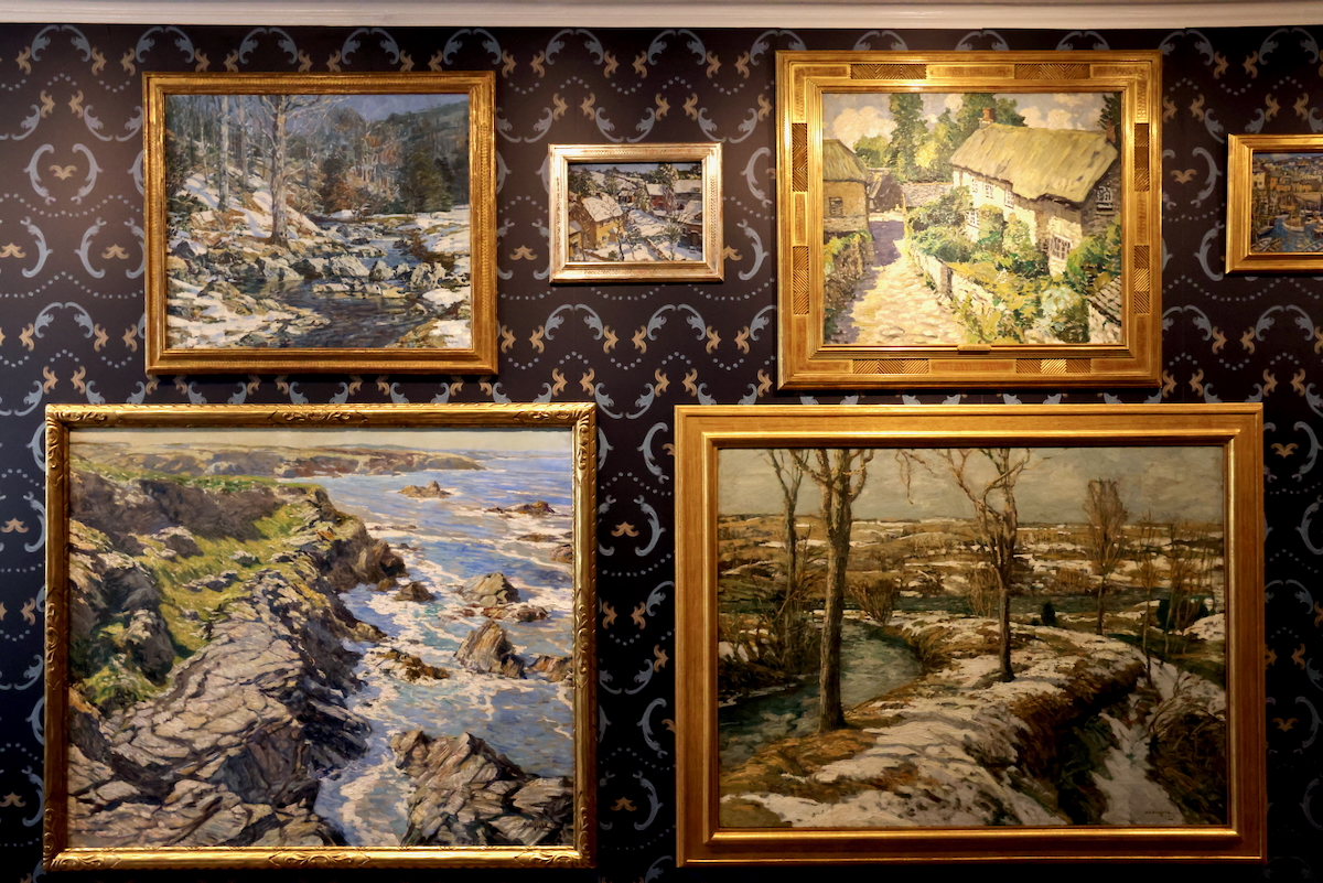 Numerous framed paintings on display on a wall
