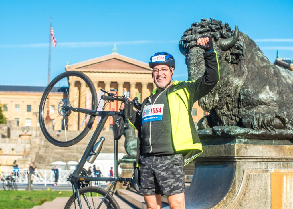 PBR-Photo7-scaled A man raising his fist and holding up his bike in front of the Art Museum steps