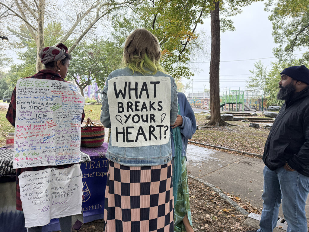 A woman wears a sign on her back that reads "What breaks your heart?"