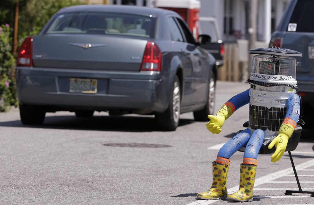 a robot sitting on a chair on the side of the road with it's thumb up for hitch hiking