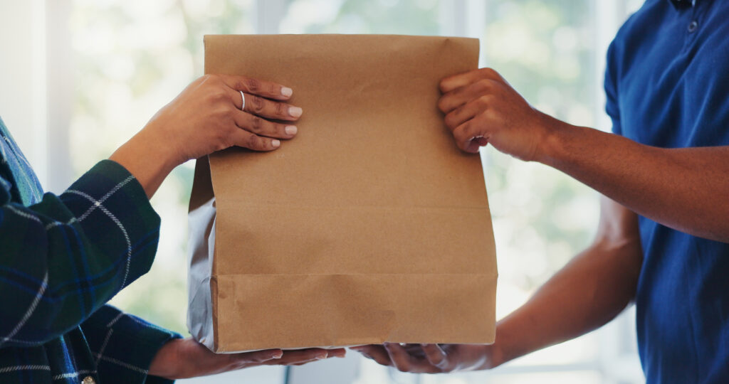 Hands, package and paper bag as delivery with customer or client order, parcel and courier. People, shopping and online with service at postal address or workplace as employee in retail and together A paper bag being handed over in a store