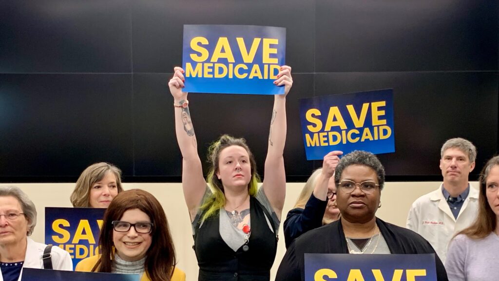 delaware-delegation-s-mueller-2025-03-17-1-file a woman in a crowd holds a sign reading SAVE MEDICAID