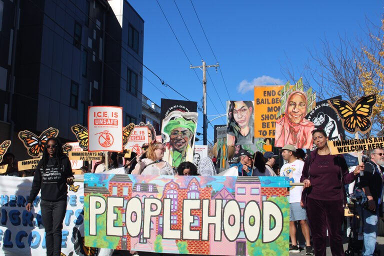 People participating in a parade in West Philadelphia hold up a sign that reads 