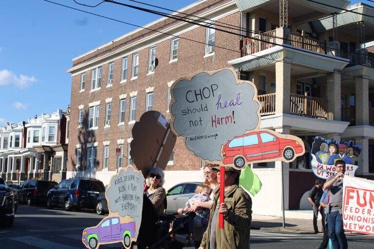 People hold up signs protesting against a proposed parking lot for the Children's Hospital of Philadelphia in the 25th annual Peoplehood Parade
