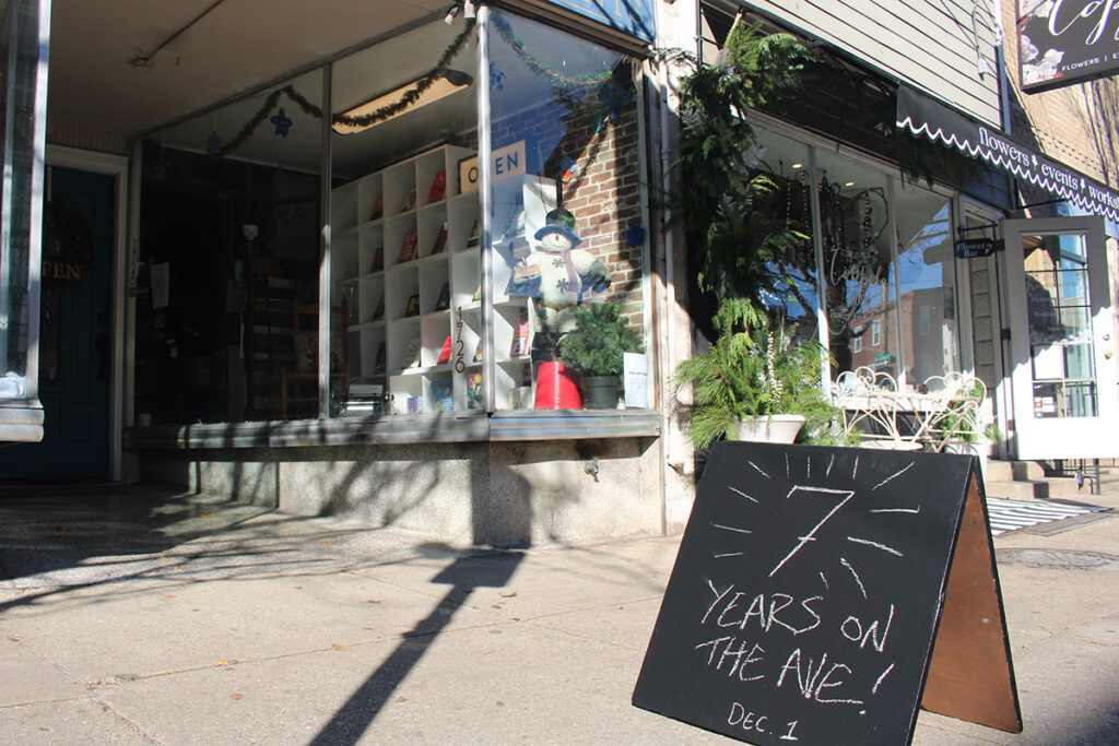 A chalkboard sign on the sidewalk reads "7 years on the Ave, Dec. 1"