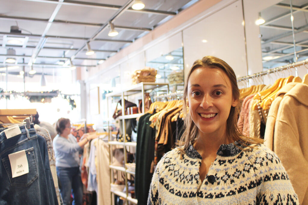 Kristina Gaglianese, the owner of August Moon Boutique, smiles at the camera in front of racks of clothes