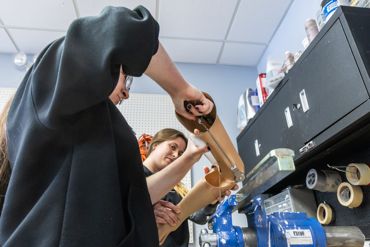 Two students are closely examining a prosthetic limb, making adjustments to it