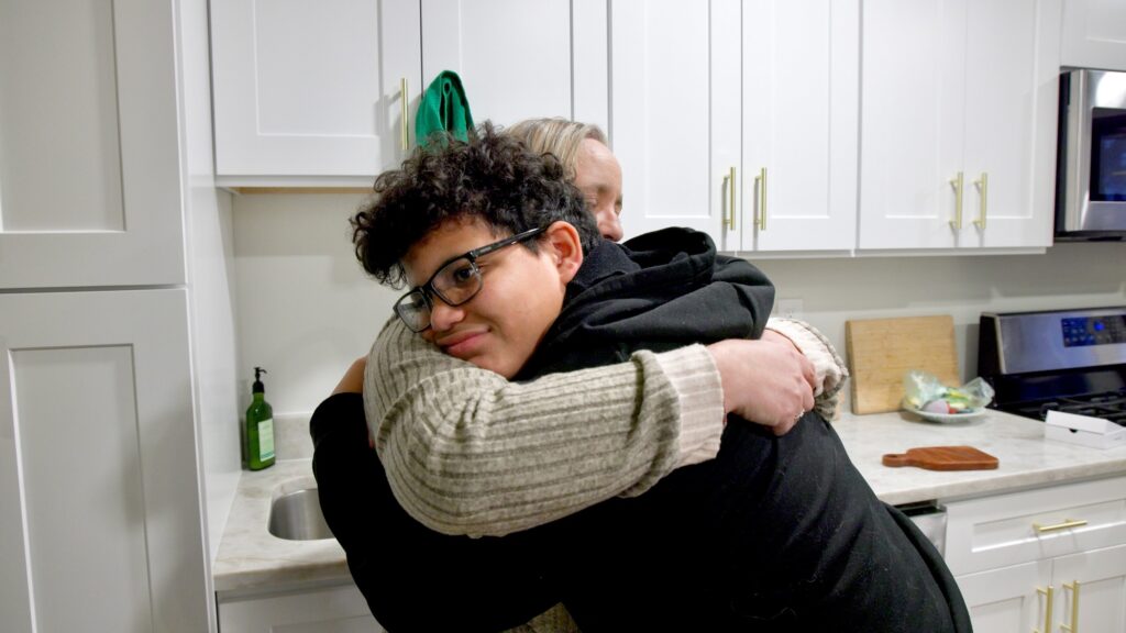 2025 12 08- elee-kelly mcglasson derek mcglasson-east brunswick nj-new jersey adoption hug A mother and son embrace for a hug in their kitchen