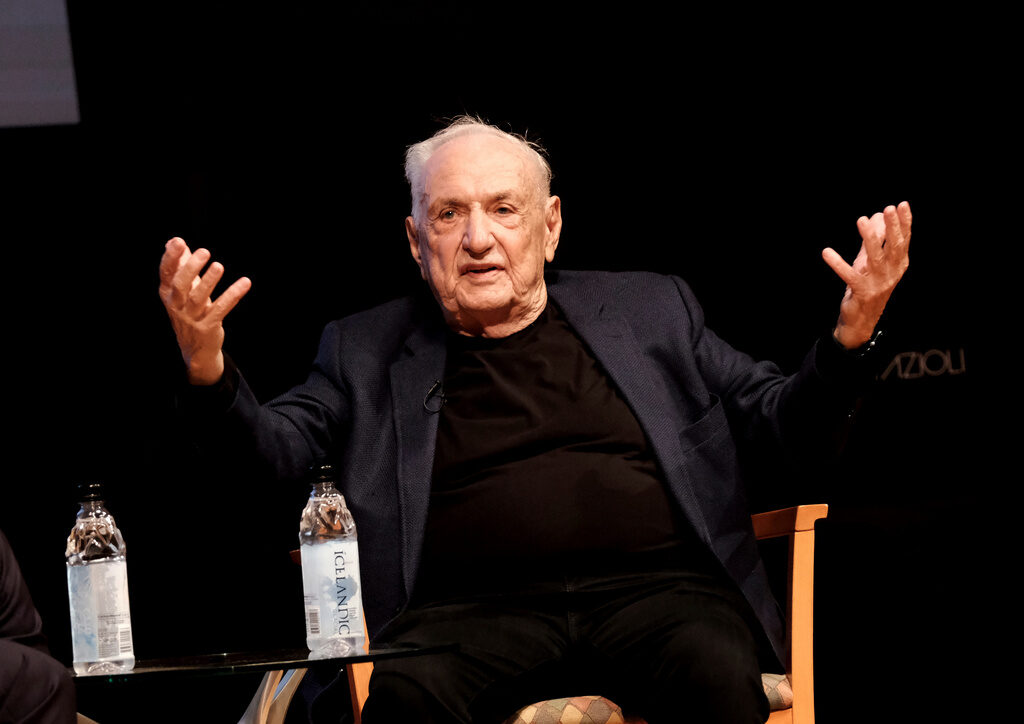 Obit Frank Gehry Architect Frank Gehry sits on a stage with his hands extended outward and upward