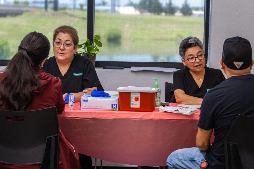 Assistant Leticia Orozco, left, and Dr. Carmen Romo, right, talk to clients while testing them for signs of diabetes during a health fair on June 6, 2025, at the Mexican Consulate in Oklahoma City. (Lionel Ramos/ KOSU)