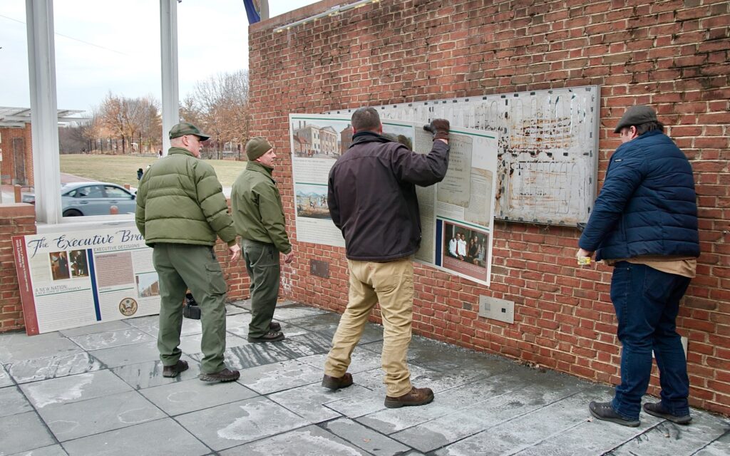 2025 01 22-e lee-philadelphia independence mall presidents house-slavery exhibit removed panel Four workers are using crowbars to remove signs from a brick wall
