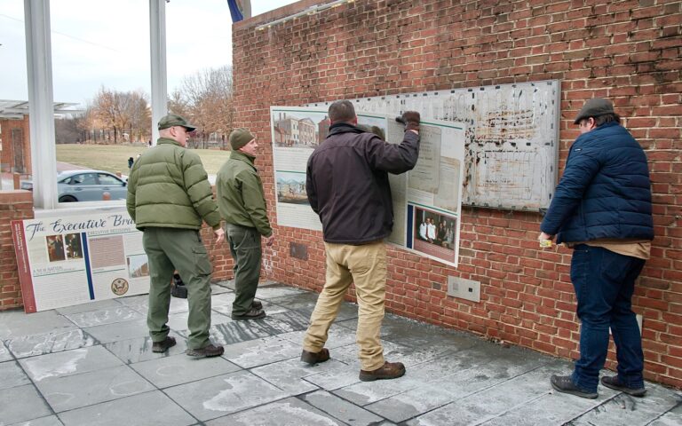 Four workers are using crowbars to remove signs from a brick wall