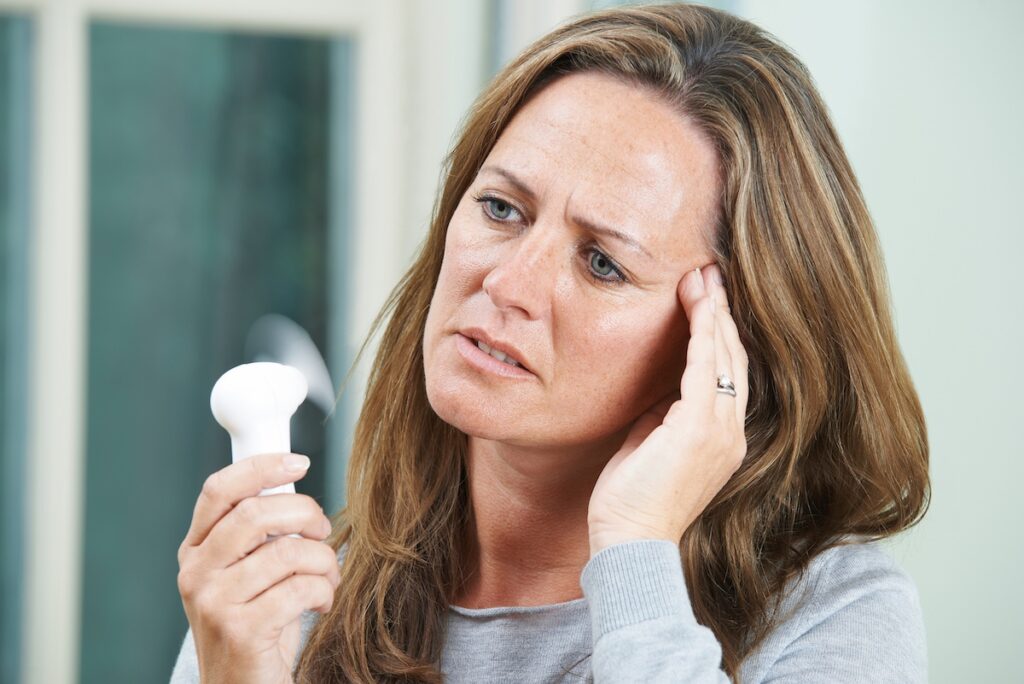 woman experiencing a hot flash, a common menopause symptom (Machineheadz/Bigstock).