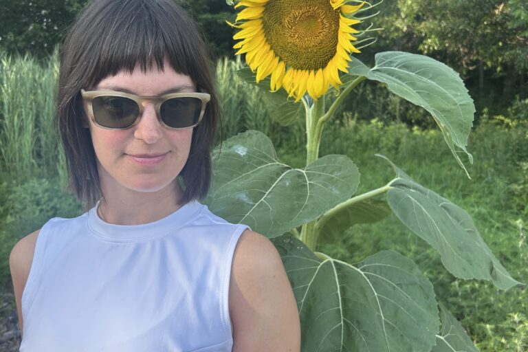 Emily Robb posing for a photo outdoors in front of a sunflower