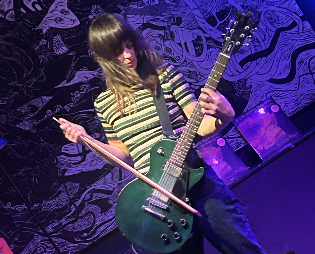 emily-robb-live-2025-01-15-2 Emily Robb using a violin bow to play her guitar during a live performance