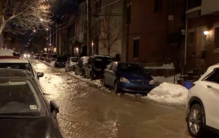 A flooded street with cars parked on either side and snow on the ground