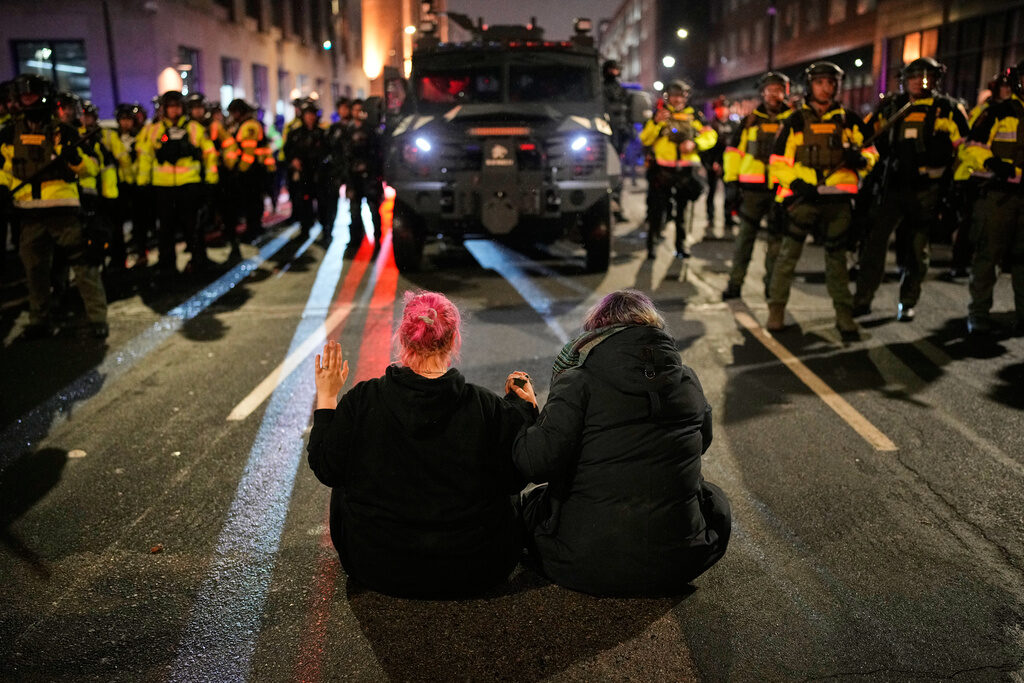 APTOPIX Immigration Enforcement Minnesota Two people sit in the street holding hands in front of Minnesota State Patrol during a protest