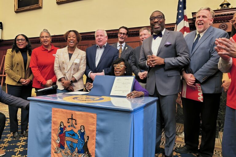 Cherelle Parker sitting at a table holding up the bill she just signed, surrounded by other officials