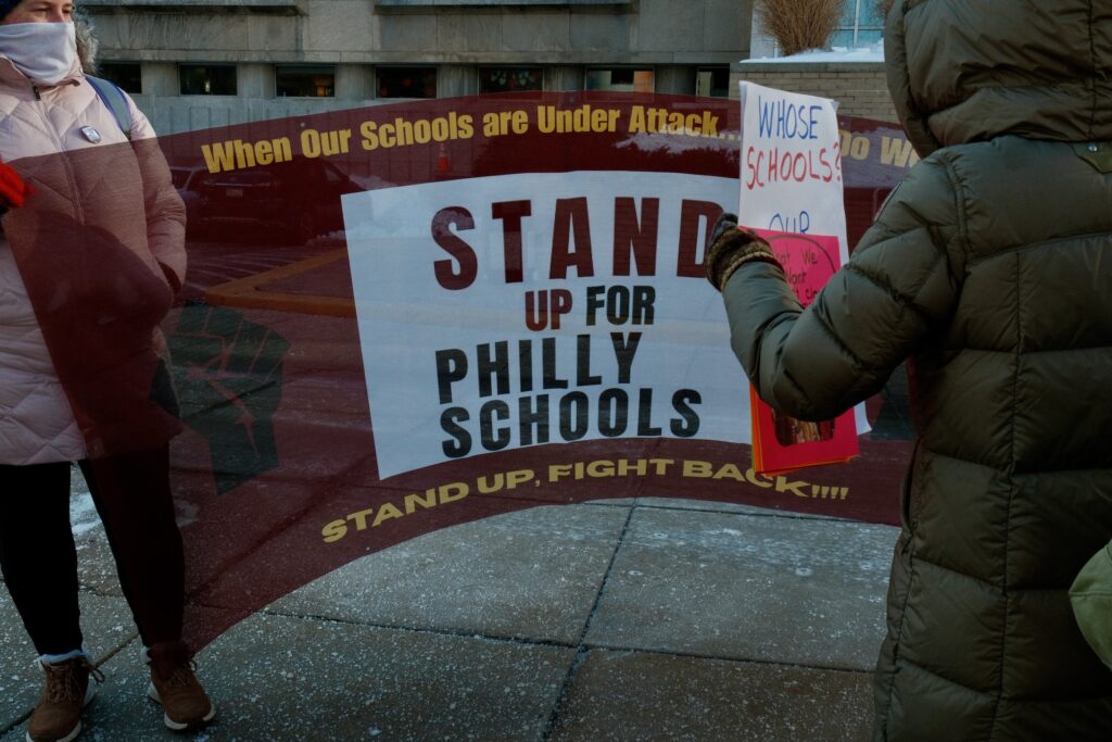 People holding up a large banner at the rally in front of the School District building