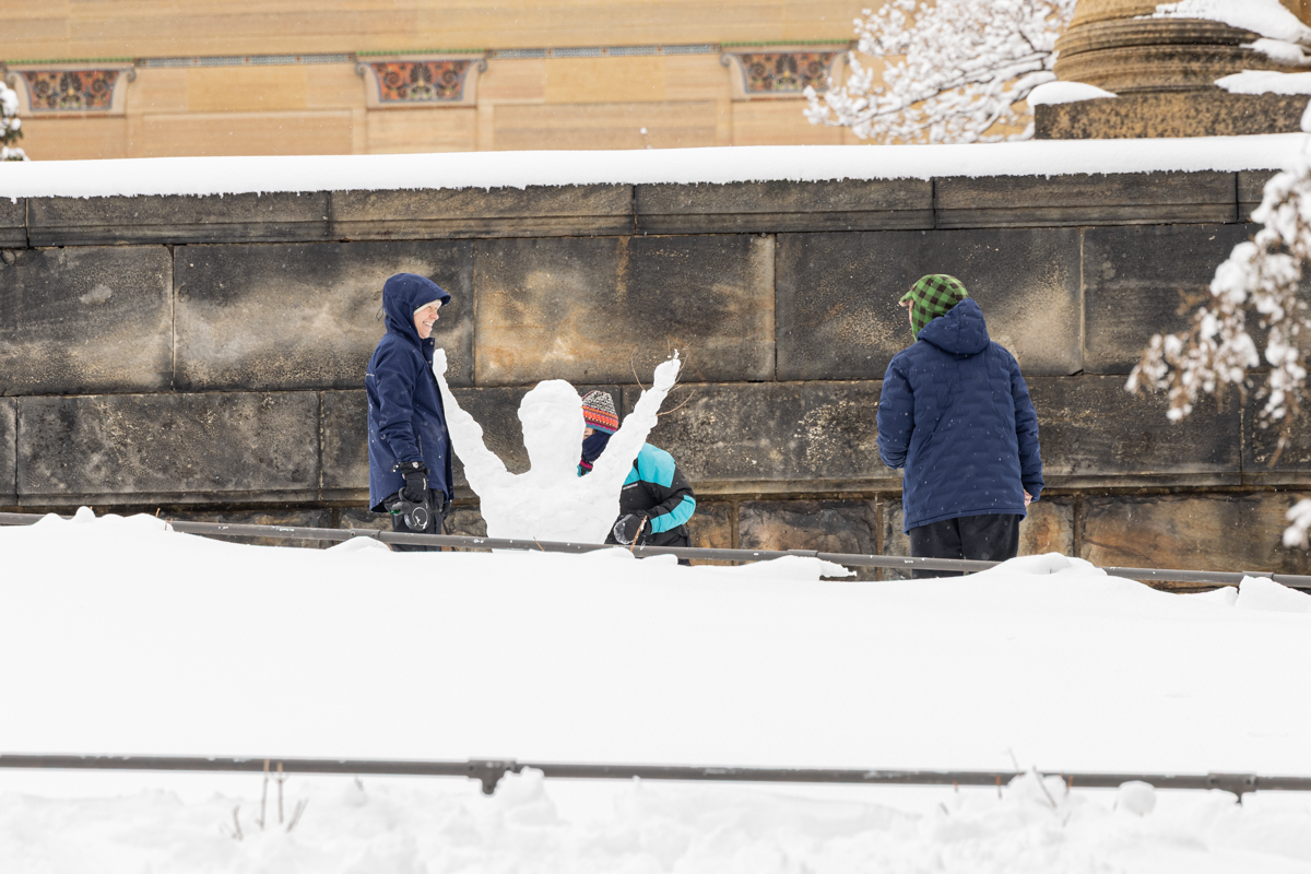 three people making a snowman shaped like the rocky statue at the Philadelphia Art Museum