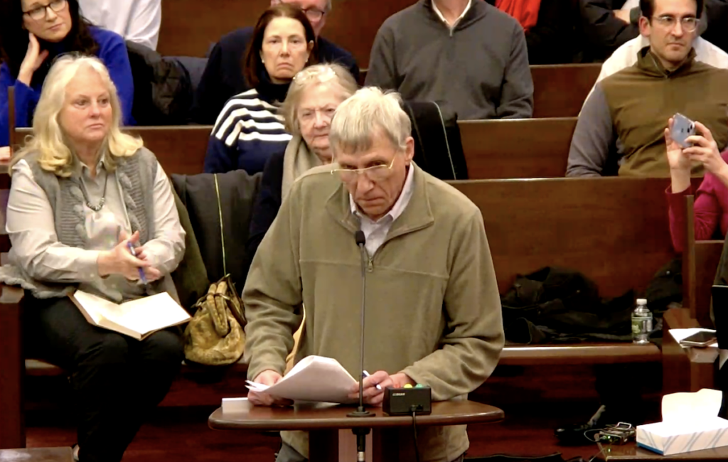 A man is standing at a podium asking a question during the meeting