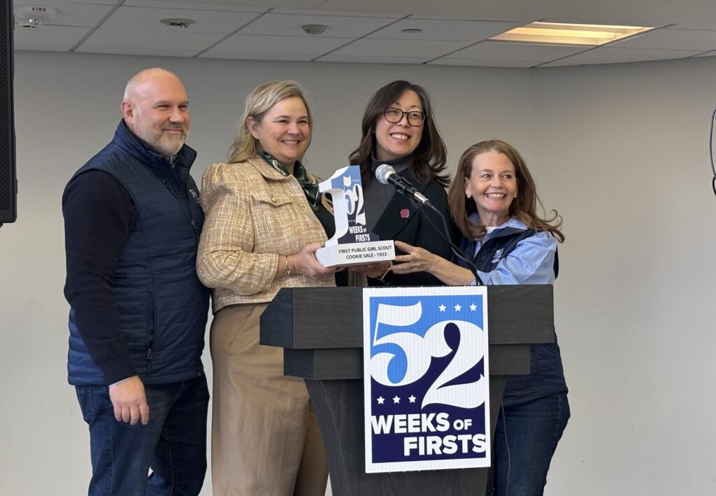Four people posing with a miniature one statue at a podium