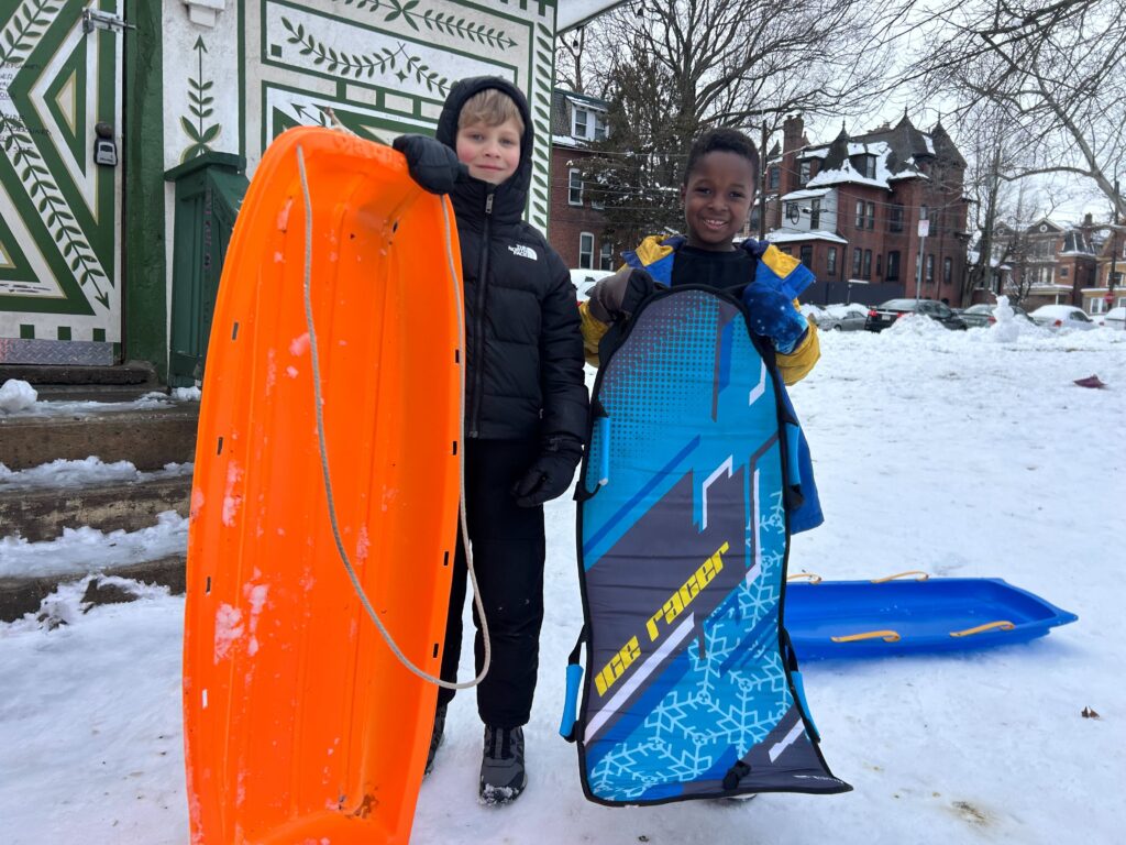 Two children pose for a photo with their sleds