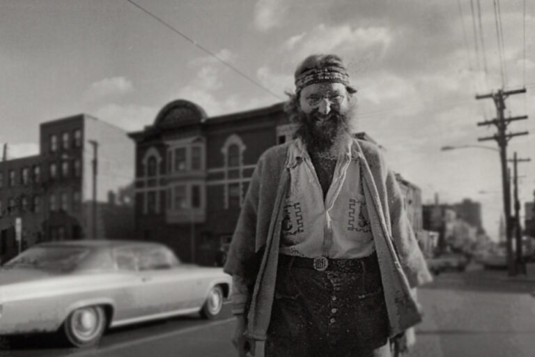 Black and white photo of Isaiah Zagar standing on a busy street corner