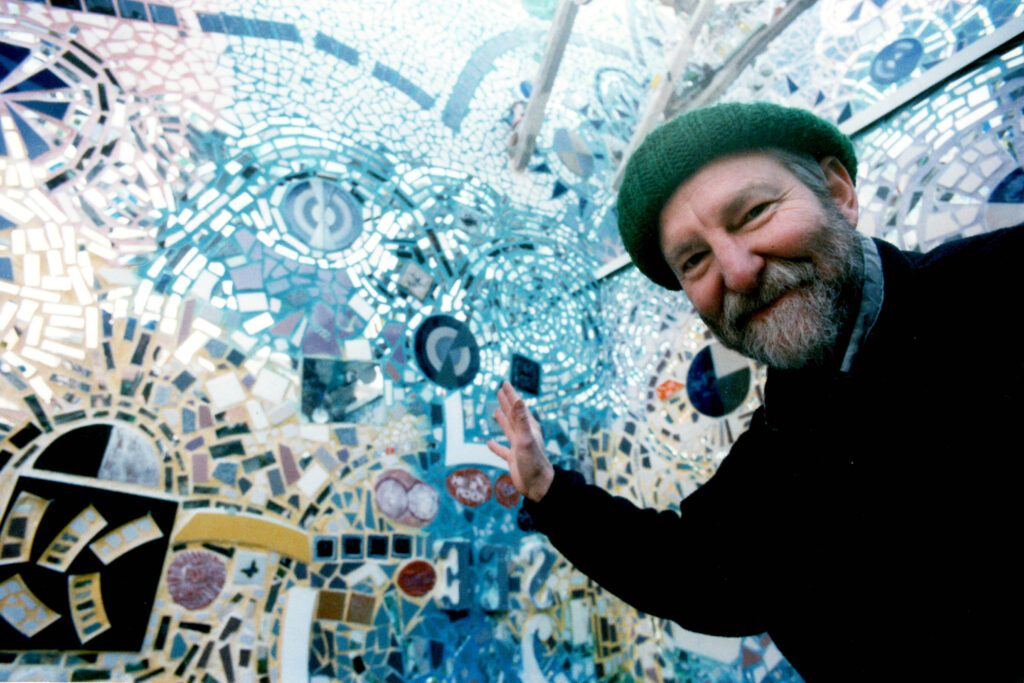 zagar-2026-02-19-Isaiah in PMG Courtyard_ late 90s Isaiah Zagar waving to the camera in the courtyard at the magic gardens