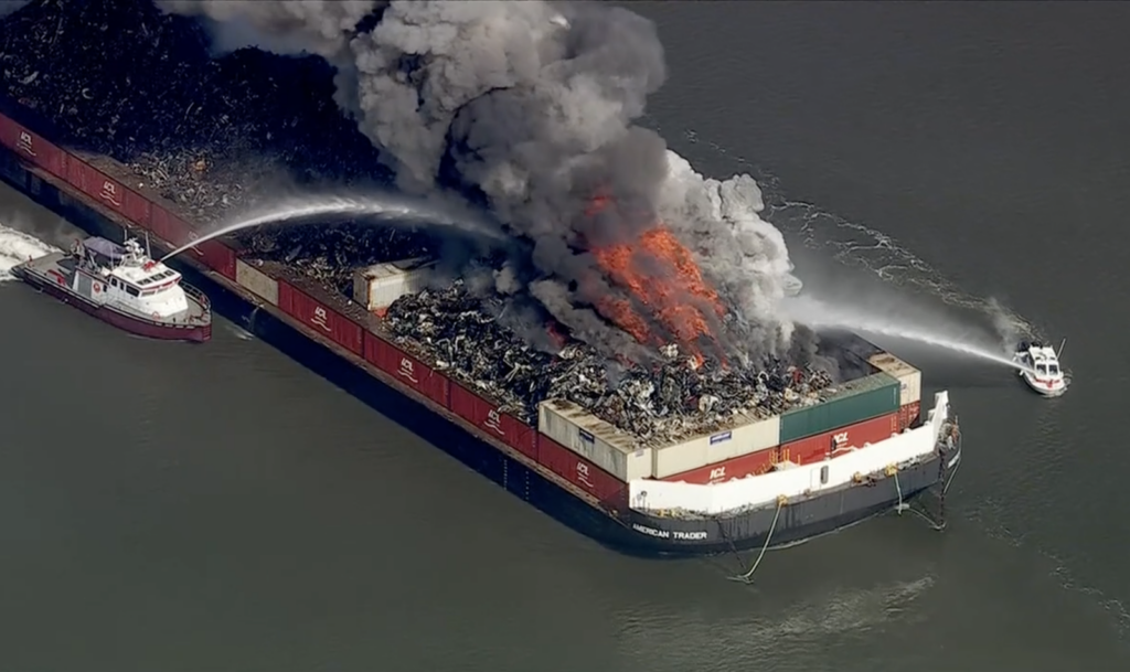 barge-fire-delaware-river-2026-03-10 a large barge is billowing smoke from a fire, while 2 small ships spray it with water to put the fire out.