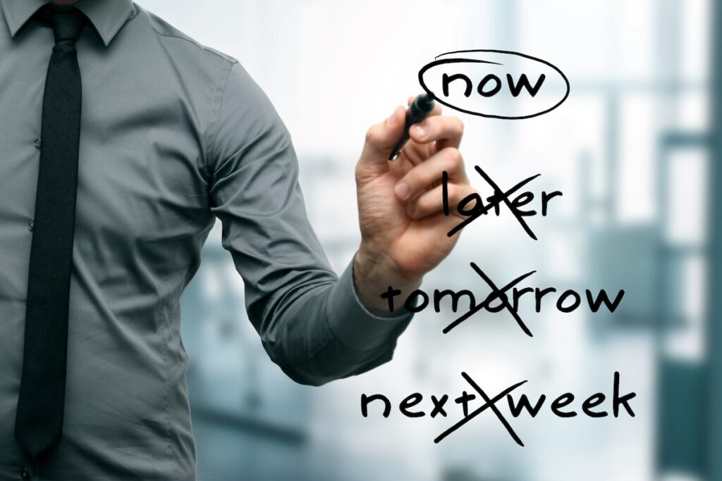 A man crosses out the words later, tomorrow and next week. He circles the word, now.