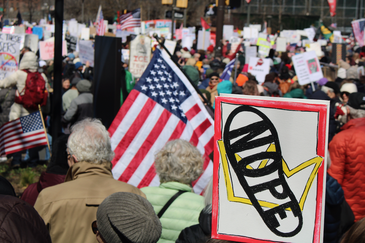 People march in Philadelphia while a sign in the foreground reads 