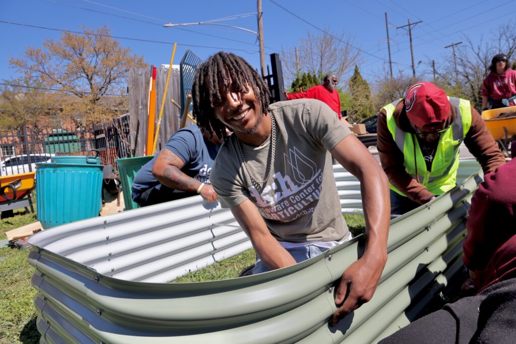A man smiles at the camera while helping assemble a raised bed in Delaware