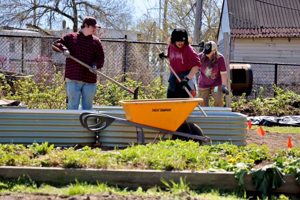 2026 04 08-e lee-elijah lewis koren weiss-wilmington del ed robinson urban garden-branches to chances rakes Three people work on plants outside in Delaware