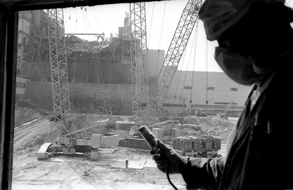In this 1986 photo, a Chernobyl nuclear power plant worker holding a dosimeter to measure radiation level is seen against the background of a sarcophagus under construction over the 4th destroyed reactor, Ukraine.
